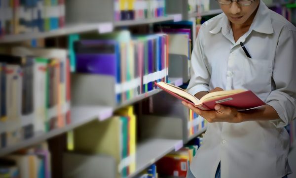 man with book in front of book shelves