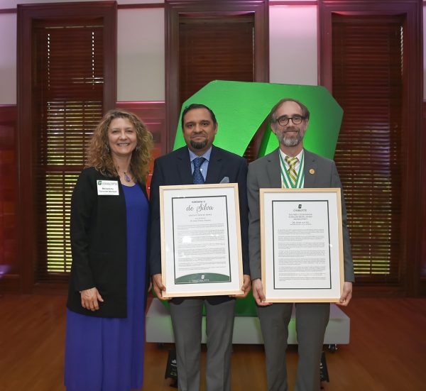 The College of Science interim dean stands with the two award winners holding their large plaques.