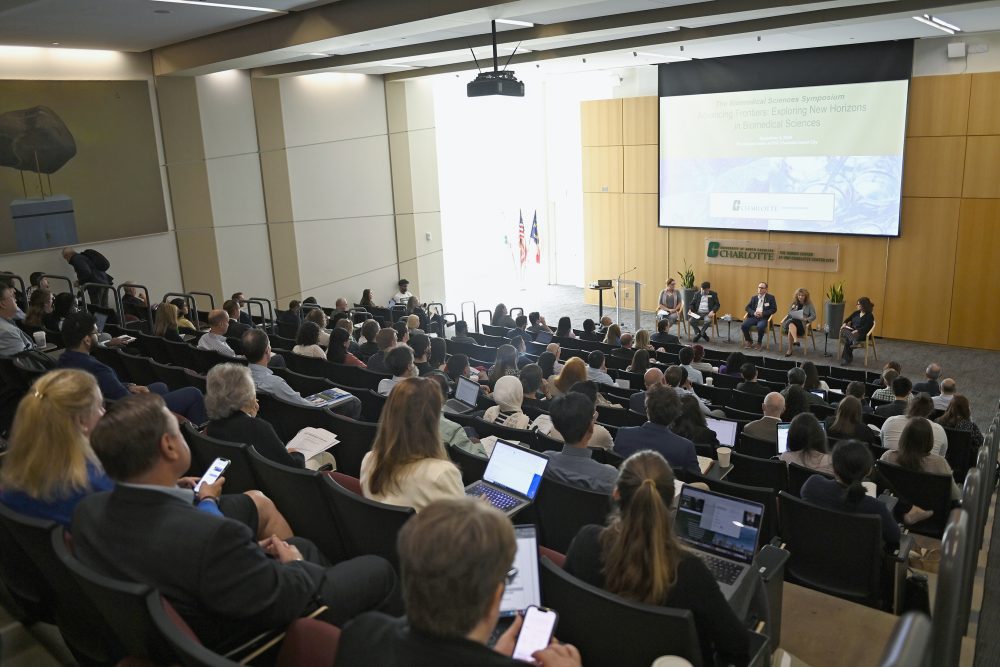 The morning session with hundreds of attendees in the auditorium look down on the panelists from the colleges.