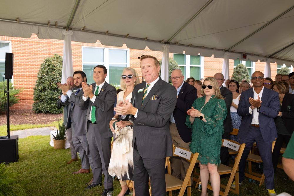 A large crowd under a tent smiles and claps.