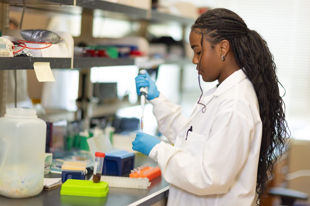 A researcher in a lab coat uses a pipette tool.