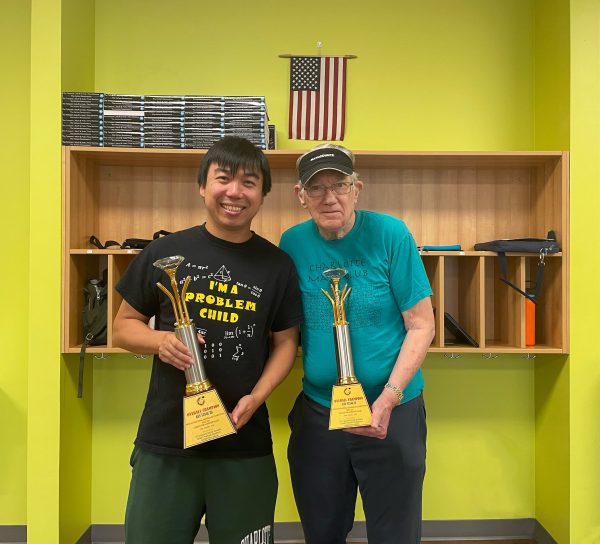 Two faculty members wear math t-shirts "I'm a problem child" with math problems and "Charlotte Math Club" while holding the Overall Champion trophies for Key stage II and Key Stage III.