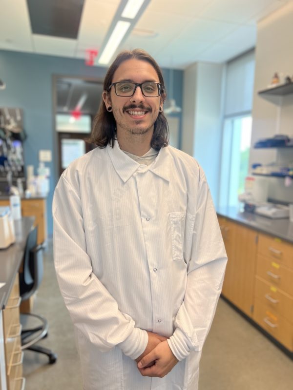 Alex Suptela wears a lab coat and smiles in the lab.