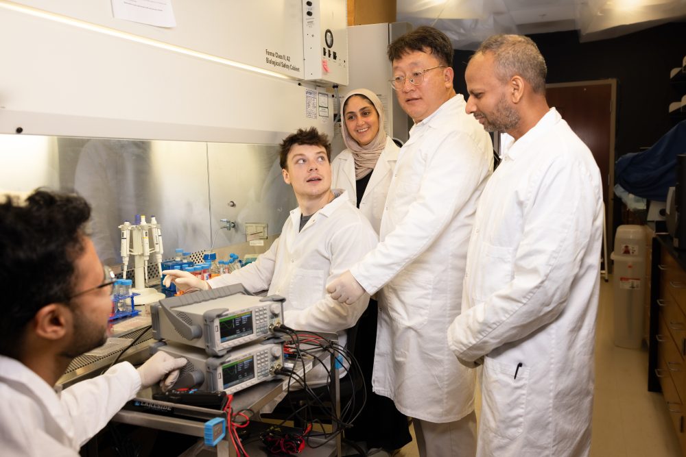 Students and faculty in lab coats working in front of a lab hood.