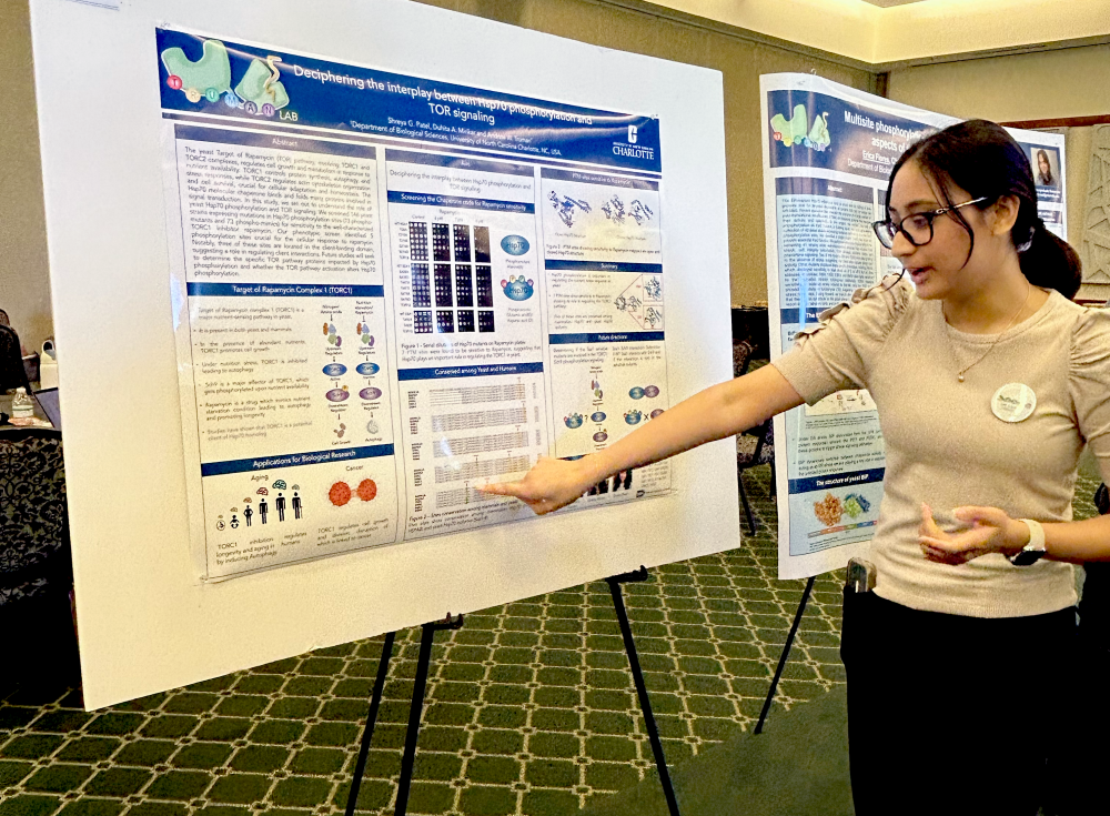 Patel presenting her research poster at the Biological Sciences Symposium. She is pointing to the poster and speaking.