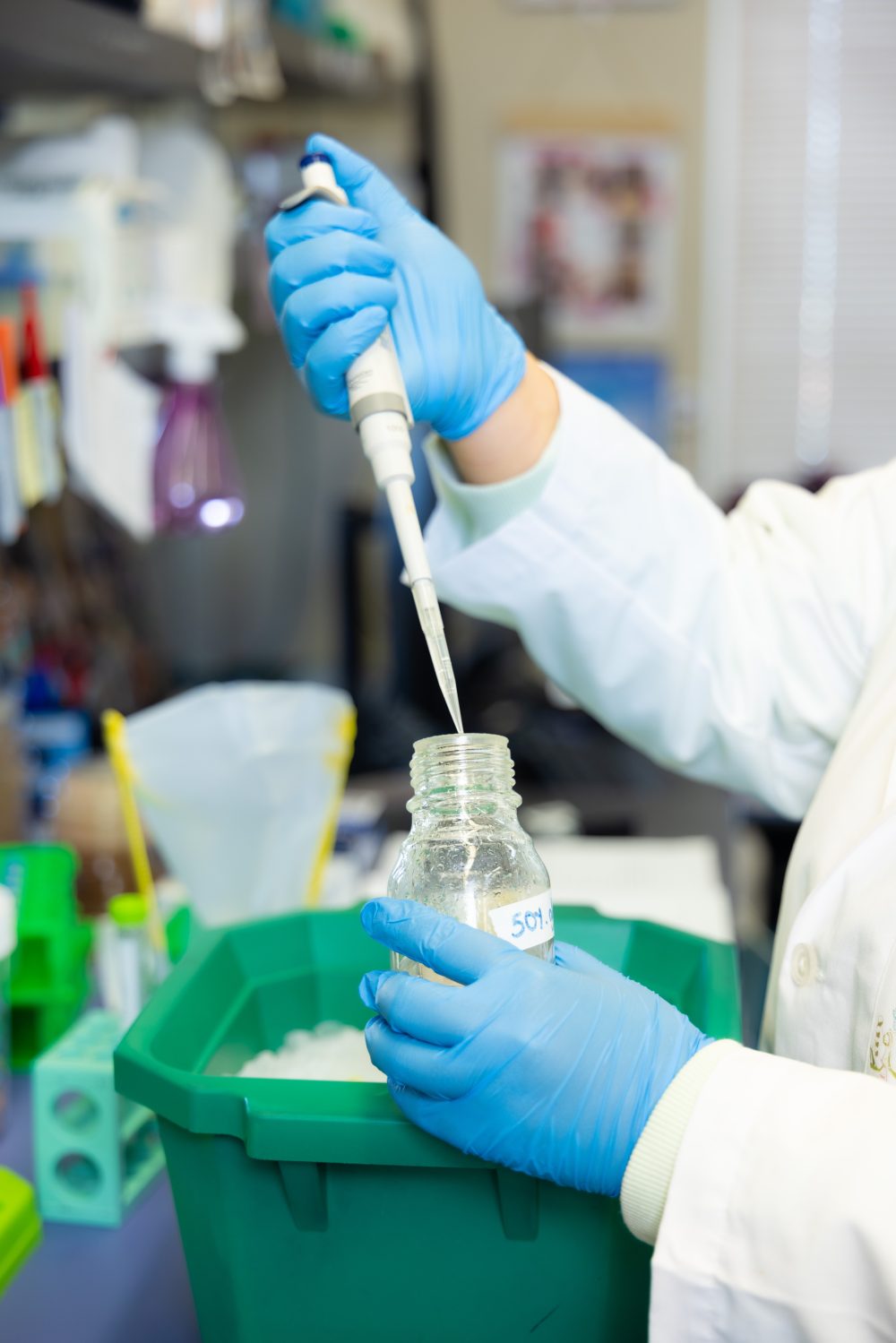 A close up shot of Choi using a pipette to add liquid to a large glass bottle. A green tub with ice can be seen in the background.