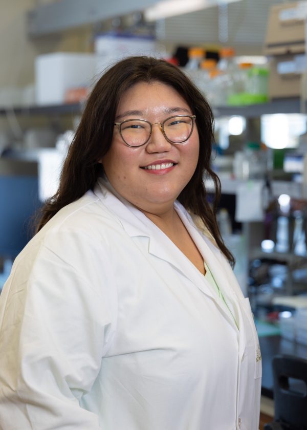 Headshot of Ashley Choi in a biological sciences lab wearing a white coat and glasses.