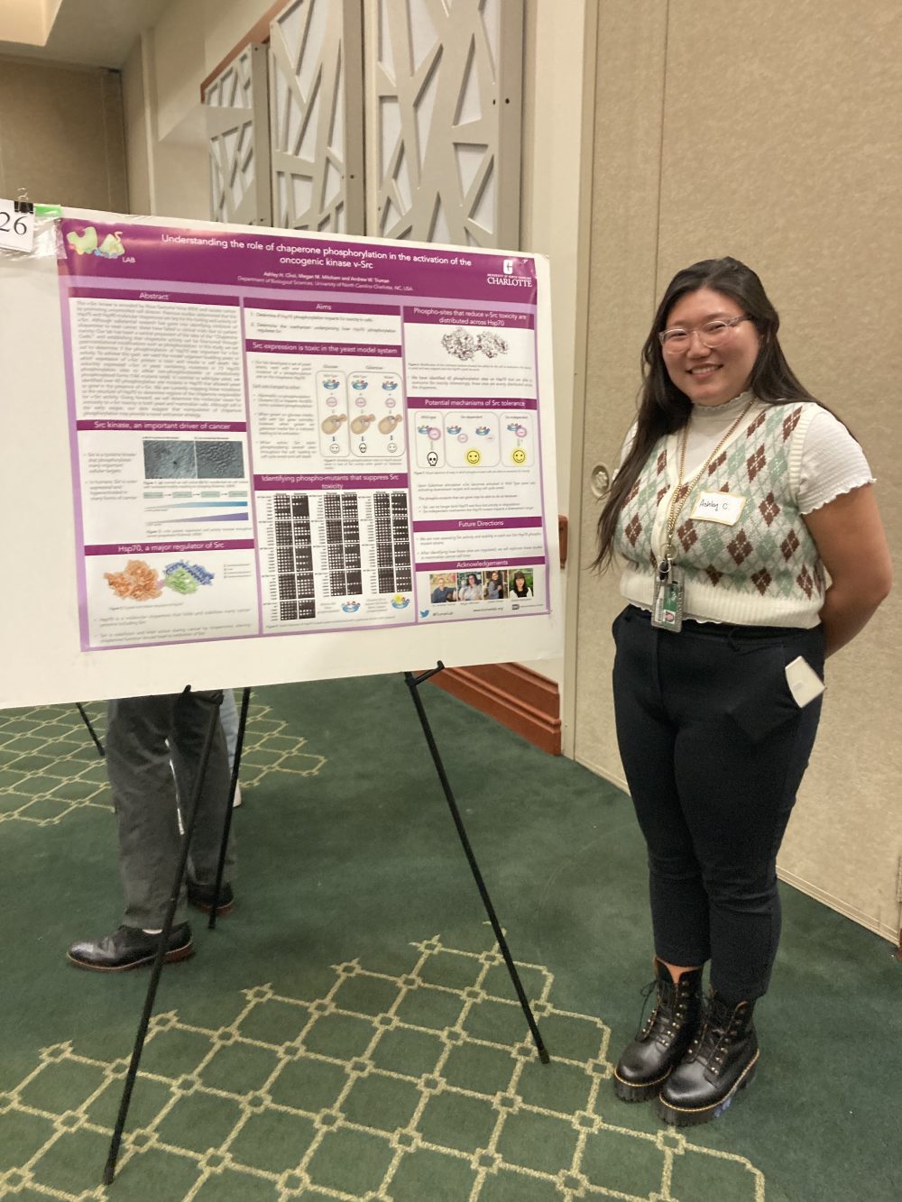 Choi standing with her hands behind her back in front of her research poster on v-Src.