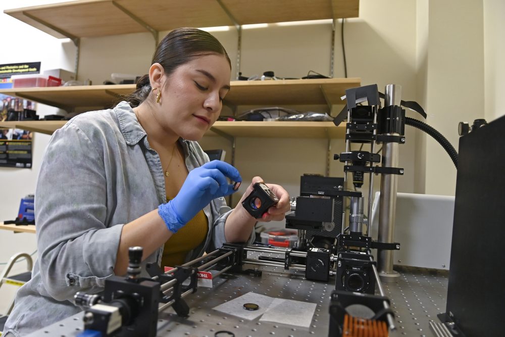A student works at a bench with optics equipment.