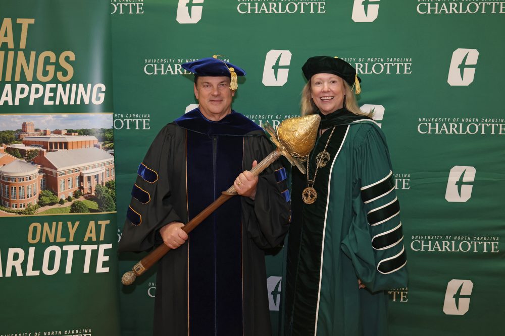 John Taylor holds the mace while standing next to Chancellor Sharon L. Gaber, in front of a UNC Charlotte backdrop.