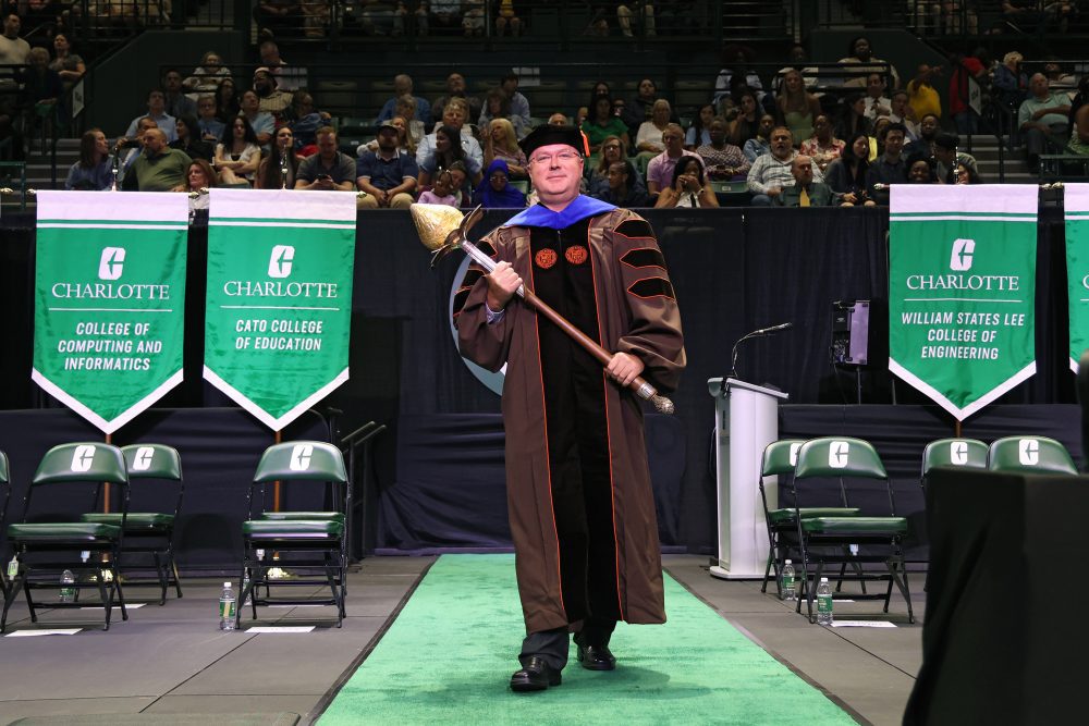 Kirill Afonin holds the mace, walking on stage at commencement while wearing graduation regalia.