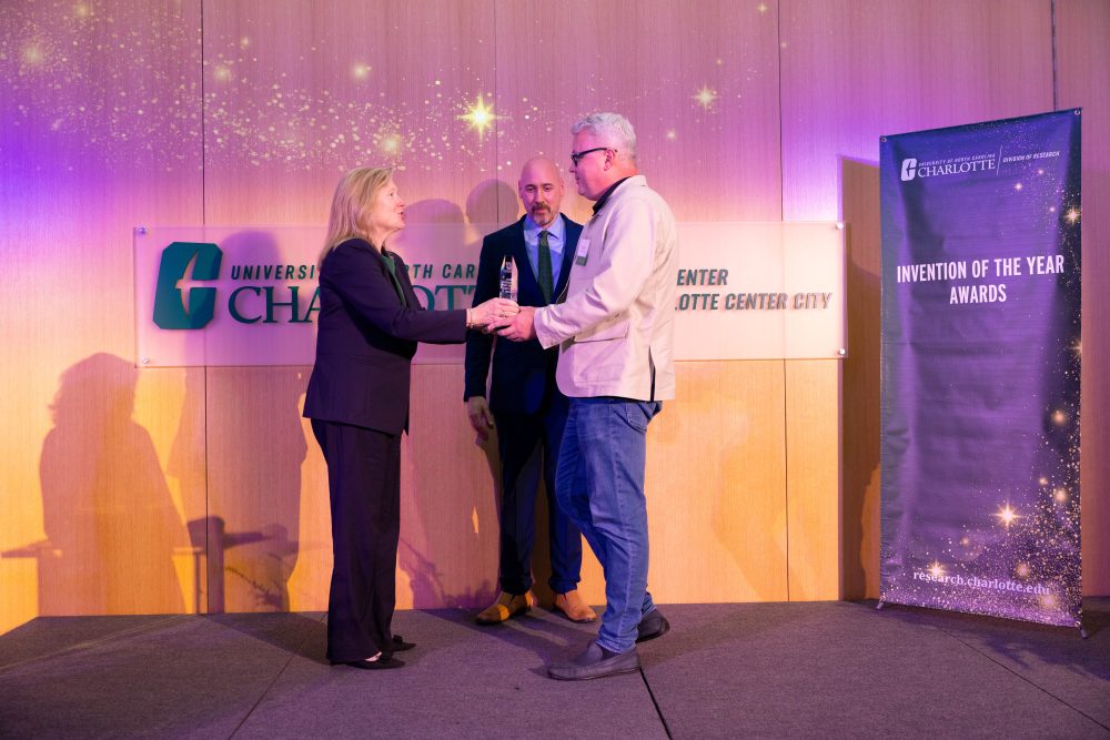 Kirill Afonin is handed his award on stage by Chancellor Gaber while John Daniels looks on.