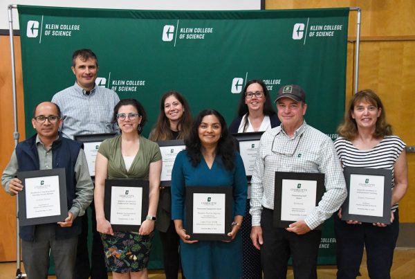 8 award winners from the Klein College of Science hold their large framed certificates.