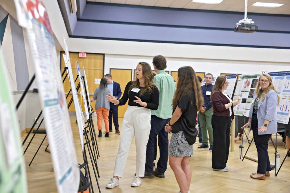 Researchers at their posters on easels speaking with attendees.