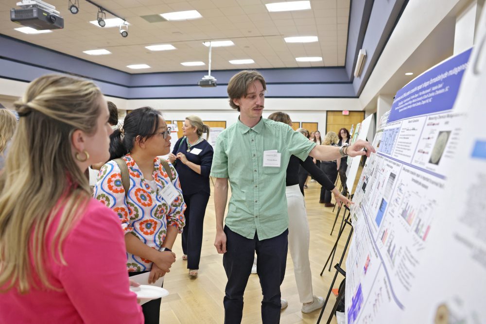 A researcher speaking in front of their poster to other attendees.