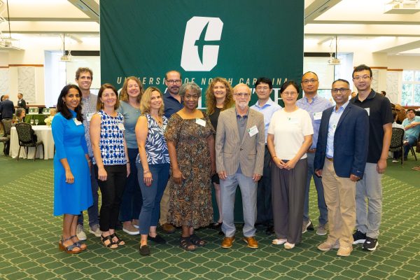 Faculty from the Klein College of Science stand in front of a UNC Charlotte background with the All-in-C.
