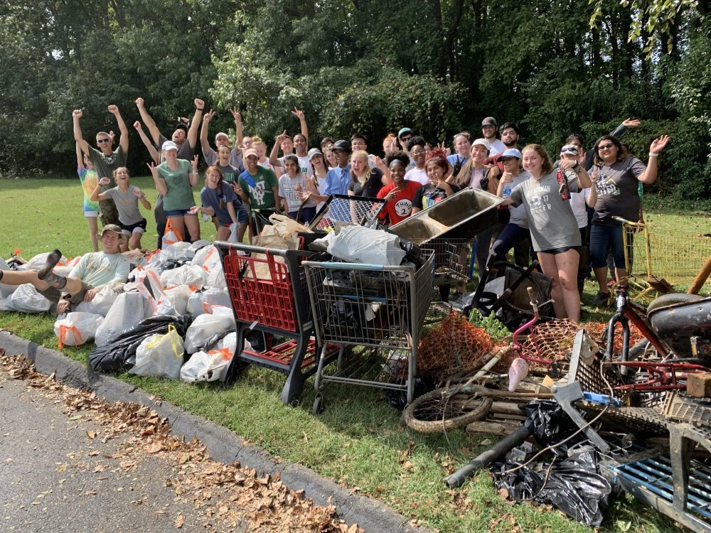 The stream clean up team is surrounded by the a giant pile of trash bags and bulk waste they collected, including several shopping carts, a bike and a sink.