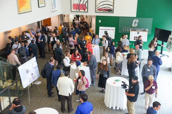 Large group of attendees gathered in the atrium at the Dubois Center, talk with each other, looking at posters and mingling.