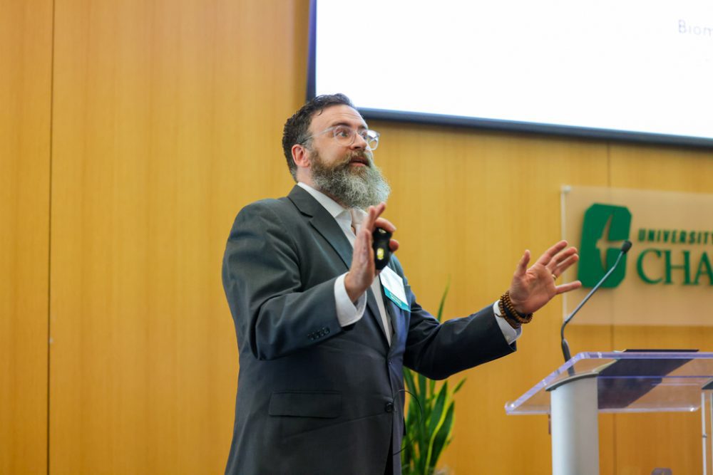 Brad Bower standing and presenting with a powerpoint clicker in his hands.
