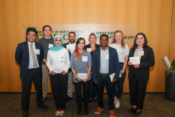 Eight students pose with their 2025 Biomedical Sciences Symposium award cards in front of the UNC Charlotte logo.