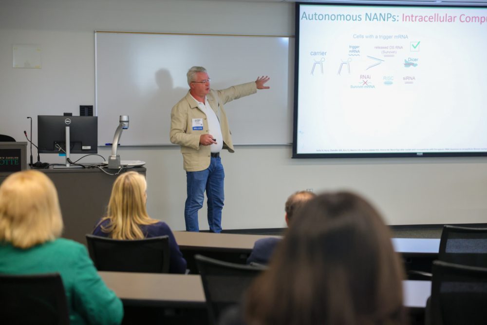 Professor Kirill Afonin presents to the audience while pointing at his powerpoint presentation.