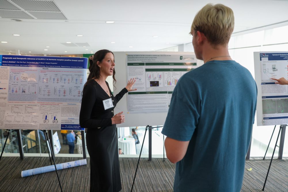 A student presenting a research poster to an event attendee.