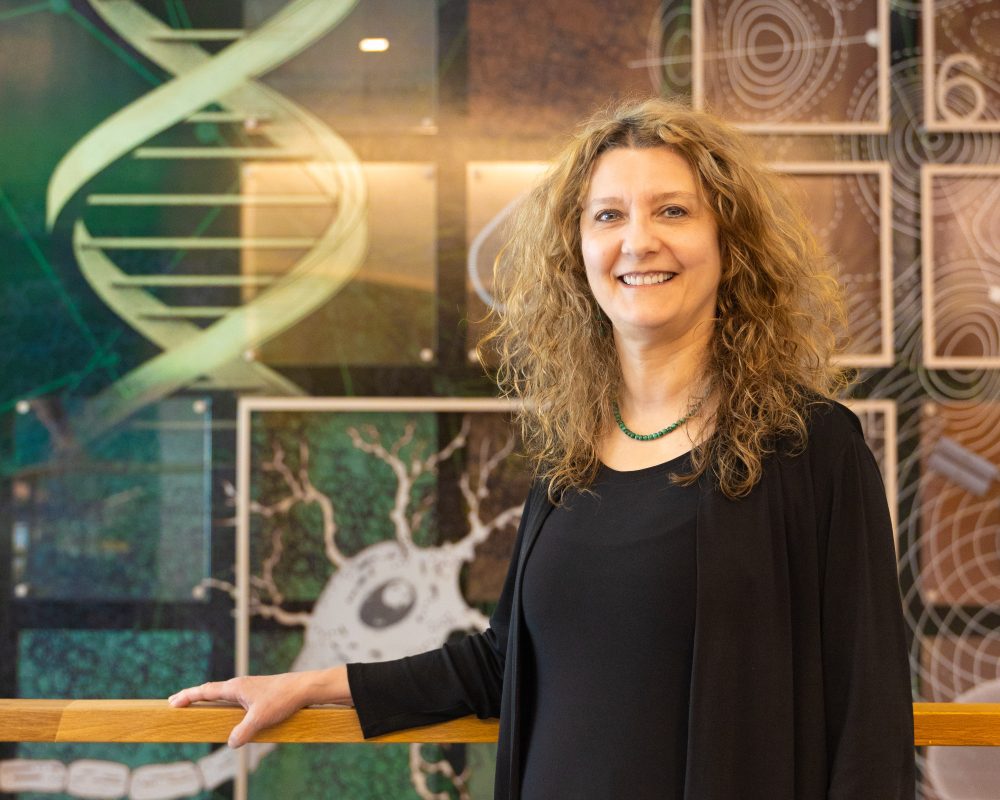 Bernadette Donovan-Merkert, founding dean of the Klein College of Science, stands in front of the art wall with science images in Klein Hall.