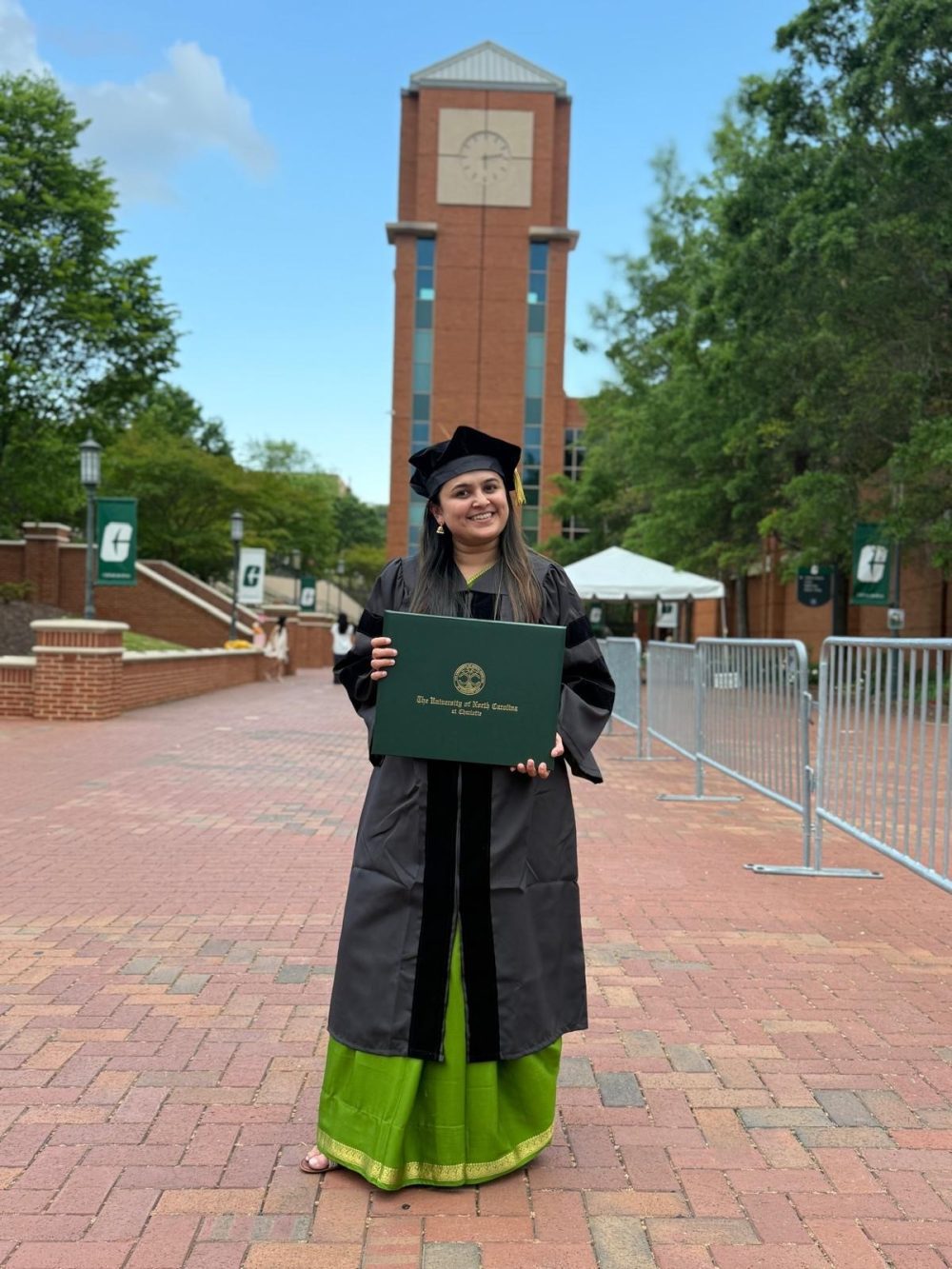 Siddhi Omkar poses in her cap and gown, holding her diploma in front of the clock tower. 