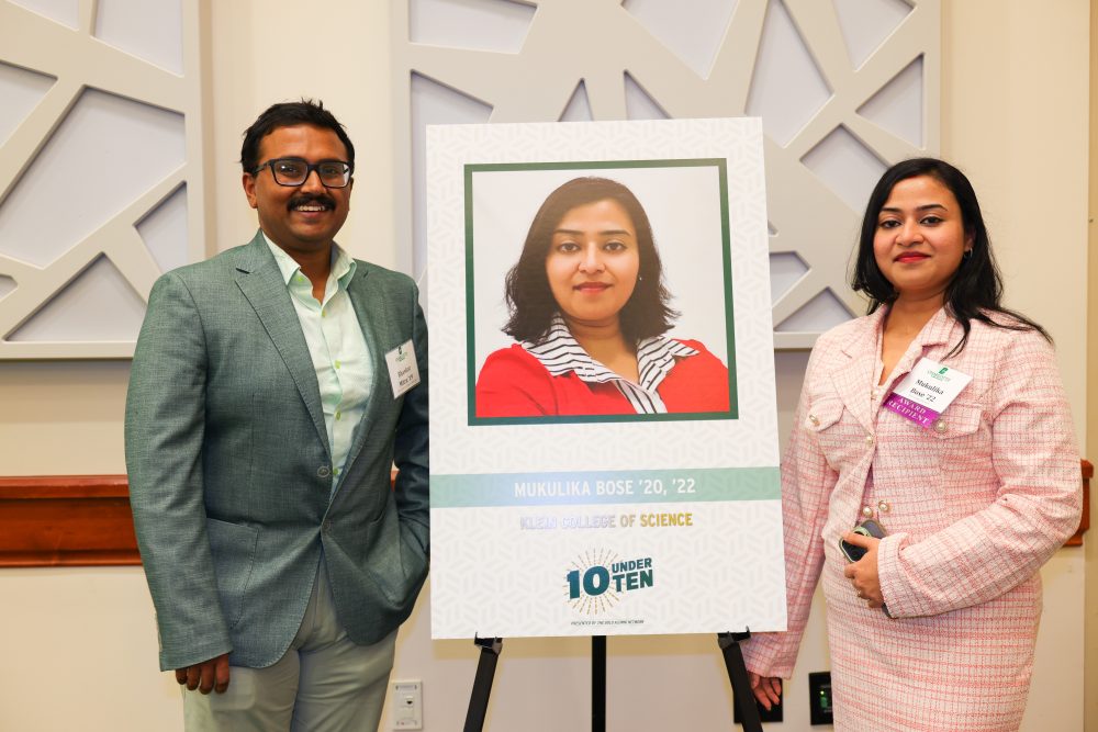 Mukulika Bose poses with family and her awad poster which features her photo and her graduation years of '20 and '22 from the Klein College of Science.
