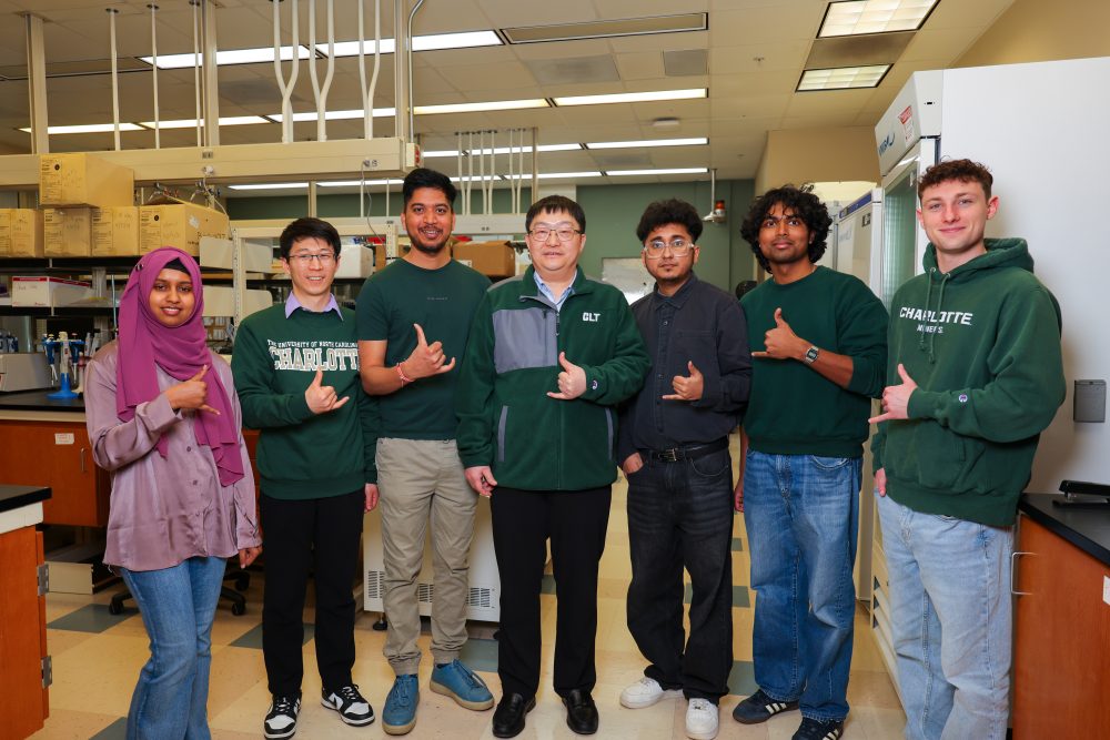 The members of the UNC Charlotte Klein College of Science Ren lab smile and show the pickaxe hand sign with their thumb and pinky finger out.