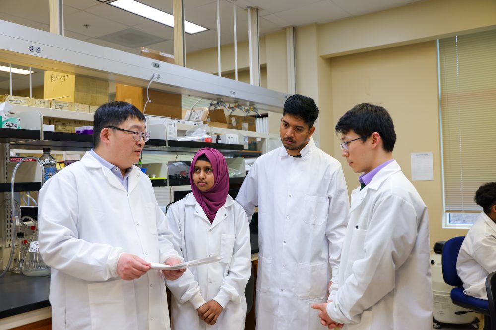 Ren lab members wear lab coats while talking in the lab.