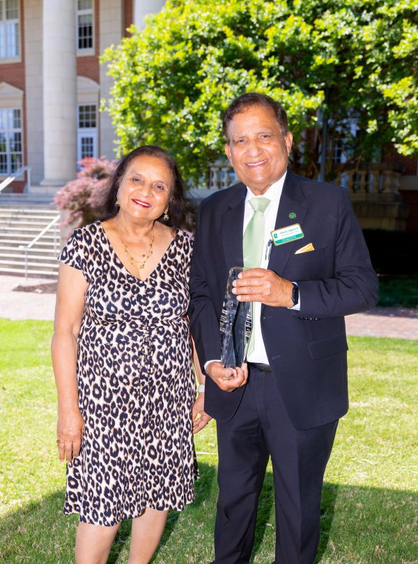 Shail Aggarwal stands with Ishwar Aggarwal, holding his gift at the naming event for the UNC Charlotte Aggarwal Department of Physics and Optical Science.