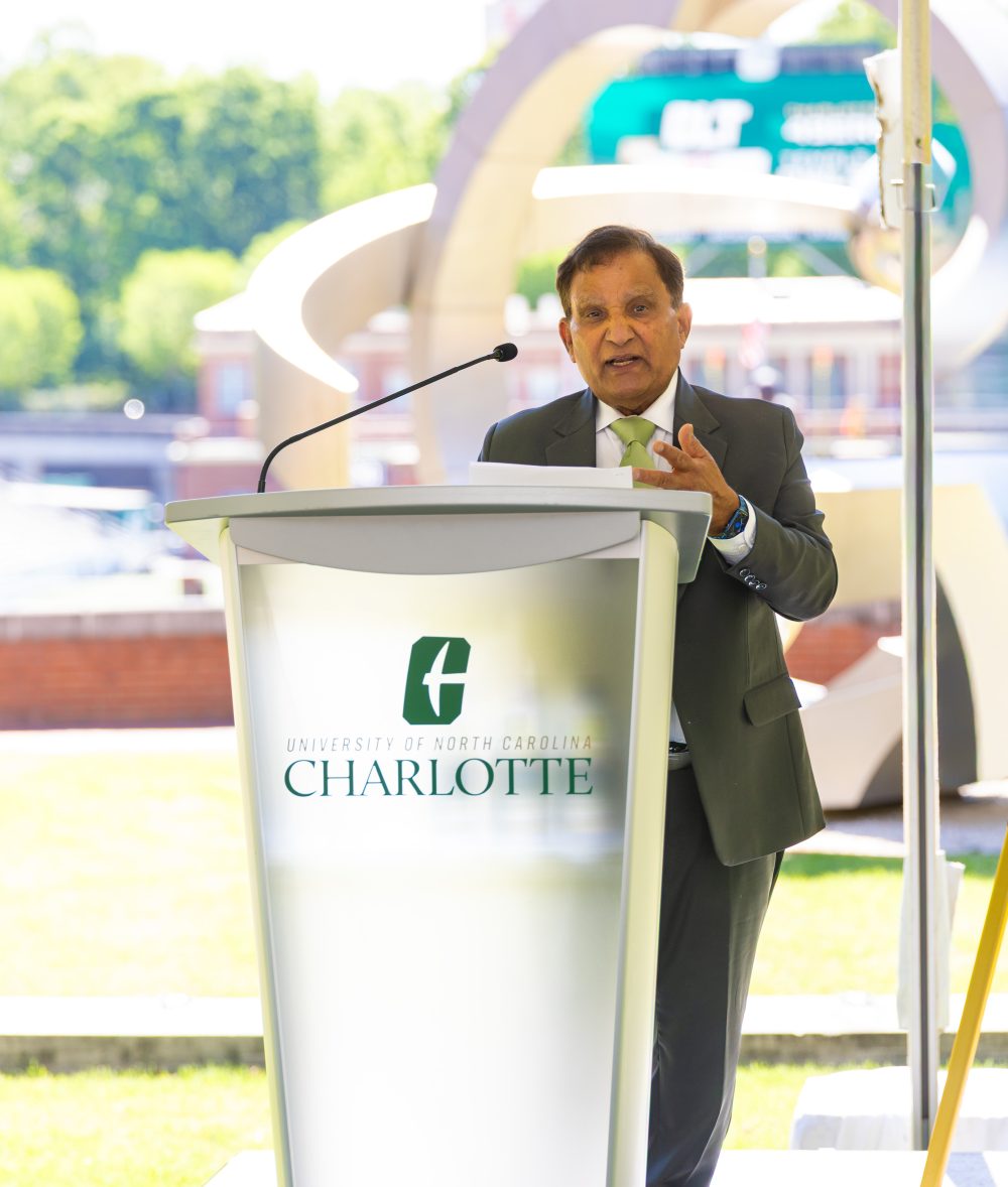 Ishwar Aggarwal speaks outside in the Gregg Hall courtyard at a UNC Charlotte podium. 