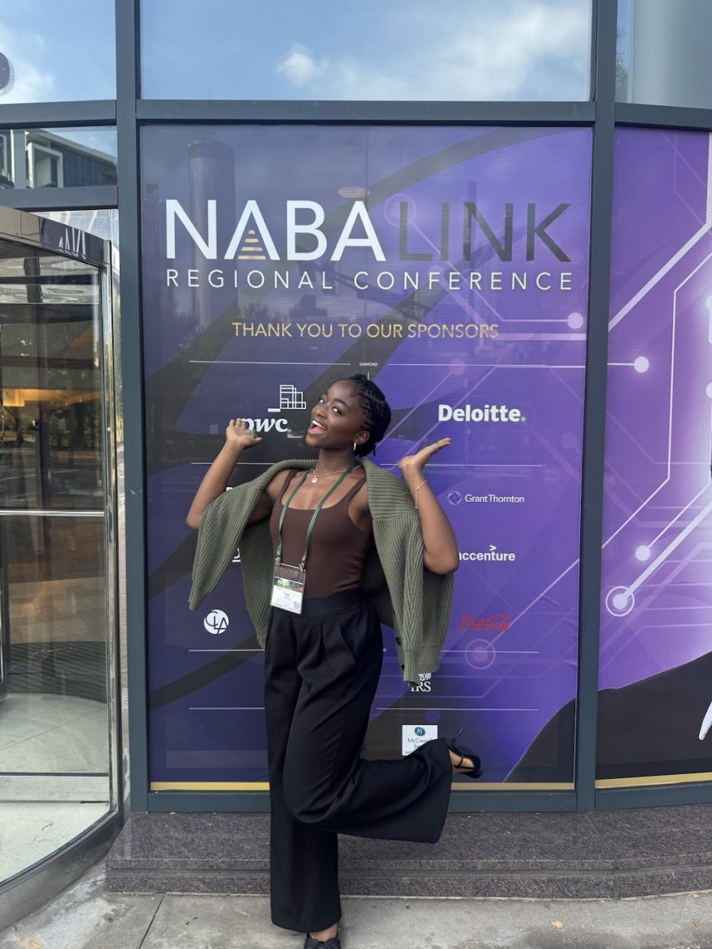 Ntasin posing in front of the NABA regional conference sign on the front of a building.