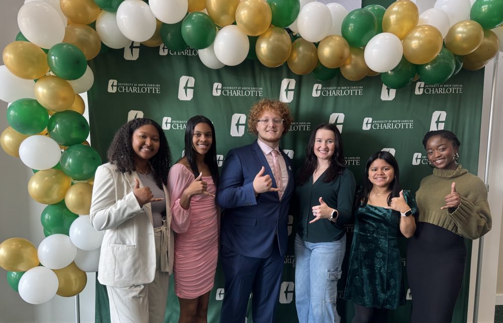 Ntasin and five Niner guides pose in front of a UNC Charlotte backdrop and balloons.