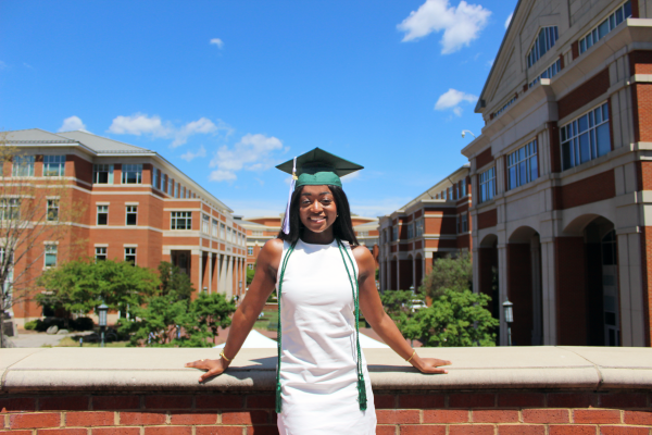 Vera Ntasin poses in white dress and graduation cap on staircase overlook above Cauble Quad.