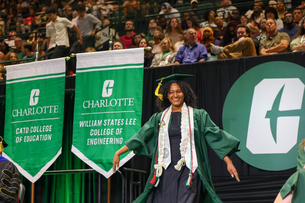 A smiling UNC Charlotte graduate from the Klein College of Science crosses the stage. 