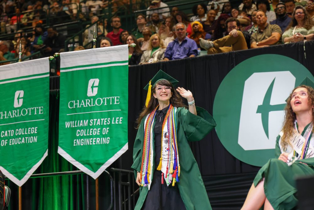 A smiling UNC Charlotte graduate from the Klein College of Science crosses the stage. 
