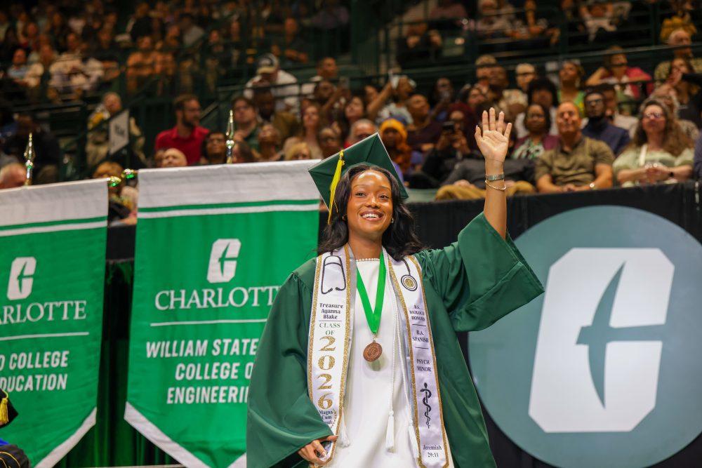 A smiling UNC Charlotte graduate from the Klein College of Science crosses the stage. 