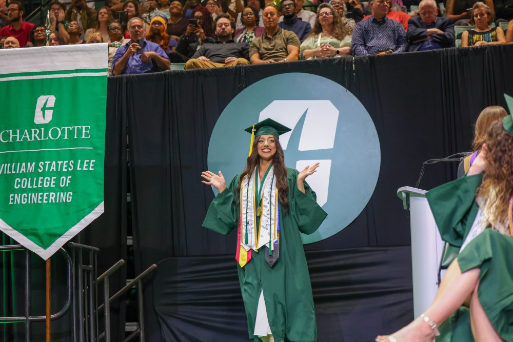 A smiling UNC Charlotte graduate from the Klein College of Science crosses the stage. 