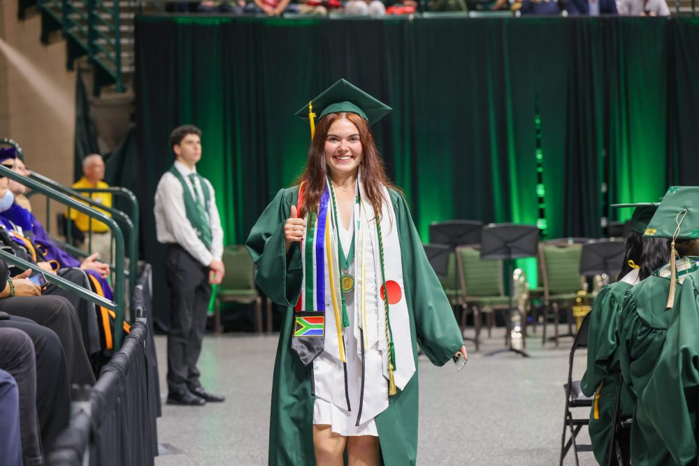 A smiling UNC Charlotte graduate from the Klein College of Science crosses the stage. 