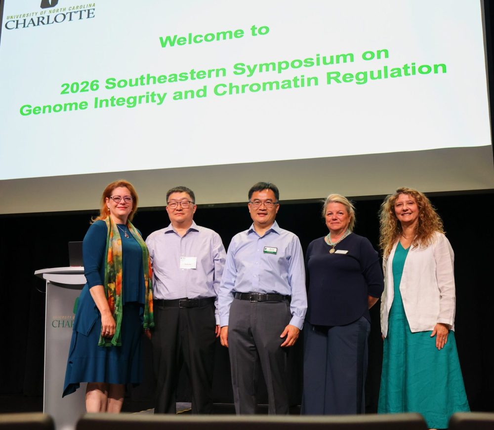 Deborah Thomas, Xiaojun Ren, Christine Richardson, Shan Yan and Bernadette Donovan-Merkert pose on the stage in front of a welcome screen.