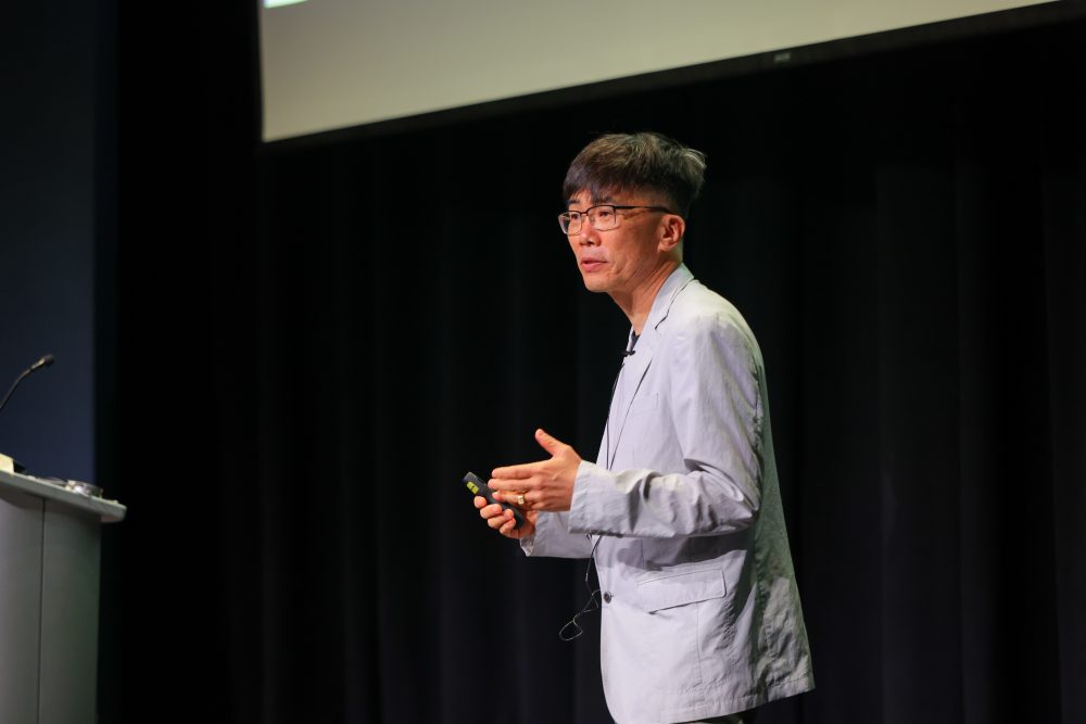 A close up of Ha on stage speaking animatedly to the crowd with both hands.
