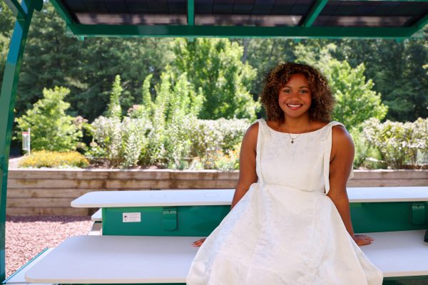 Zarah Rahman Blythe, biology major in the UNC Charlotte Klein College of Science, sits smiling on the solar powered bench between McEniry and the Pollinator Garden on UNC Charlotte's campus.