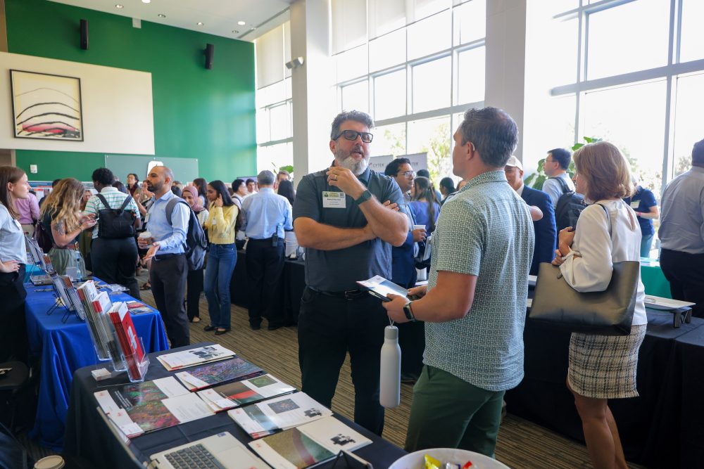 Attendees engage in conversation at the 2026 Biomedical Sciences Symposium at the UNC Charlotte Dubois Center with informational booths and displays.