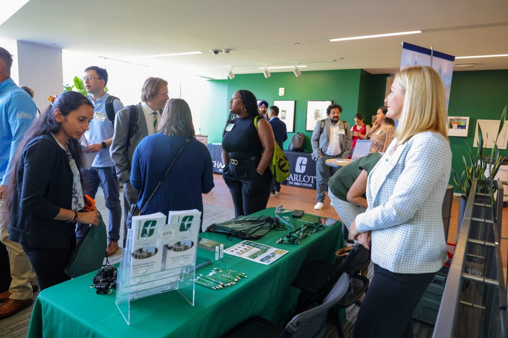 Attendees engage with a booth at an event, examining materials and interacting with a representative at a green-covered table at the 2026 Biomedical Sciences Symposium at the UNC Charlotte Dubois Center with informational booths and displays.