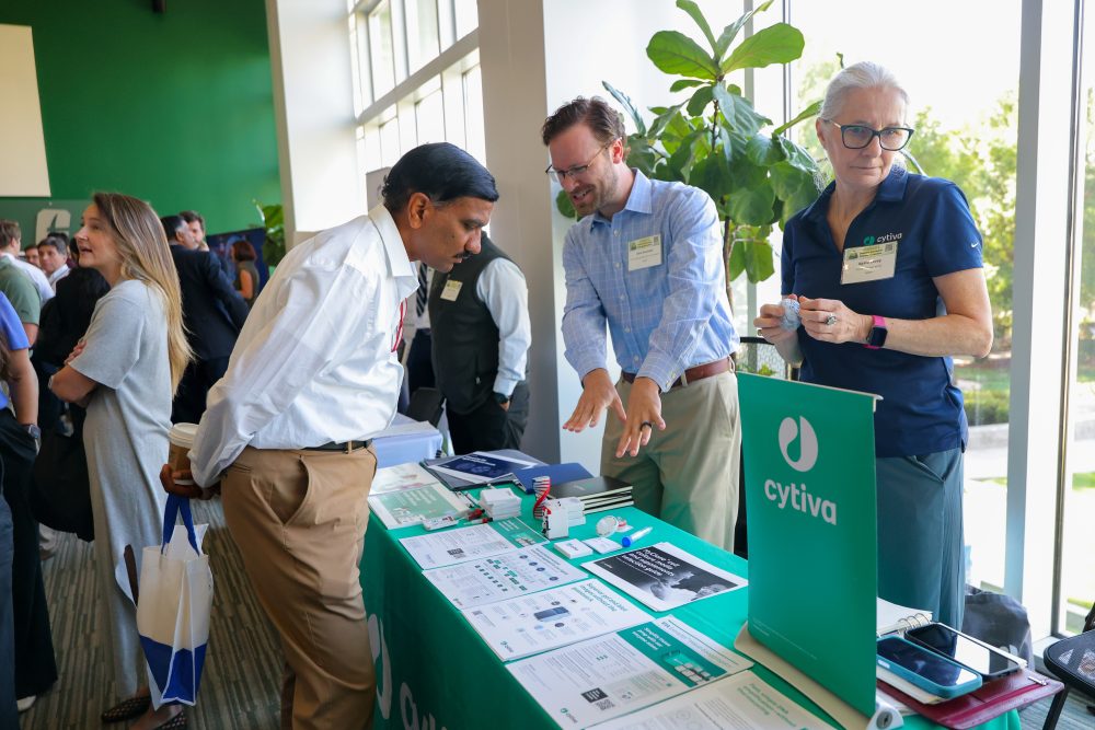 Three individuals engage with materials at a Cytiva booth during the 2026 Biomedical Sciences Symposium at the UNC Charlotte Dubois Center with informational booths and displays.