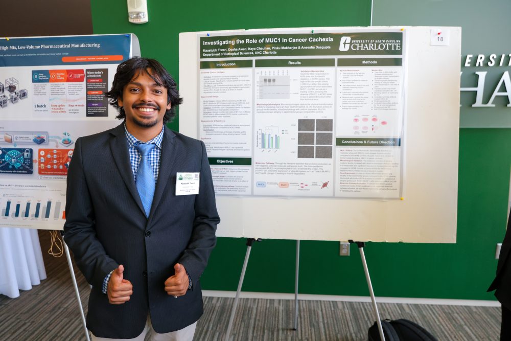 A person in a suit stands smiling in front of a research poster at a university event.