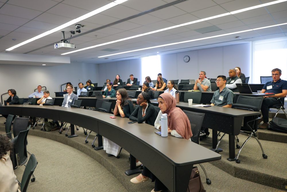 A diverse group of attendees sits in a Dubois Center lecture hall, attentively listening to a presentation.