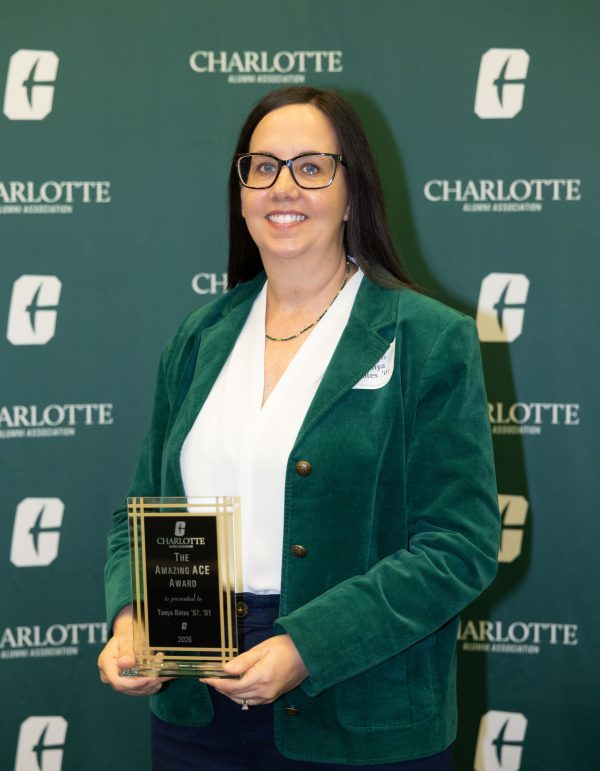 Tonya Bates wears a green blazer and stands in front of a backdrop featuring the Charlotte Alumni Association logo, holding an award plaque that reads “The Amazing Ace Award” presented to Tonya Bates '97, '01 in 2026.